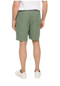 Groene gestructureerde shorts met een ontspannen pasvorm, met een achterzak, gedragen met witte sneakers, gezien vanaf de achterkant.