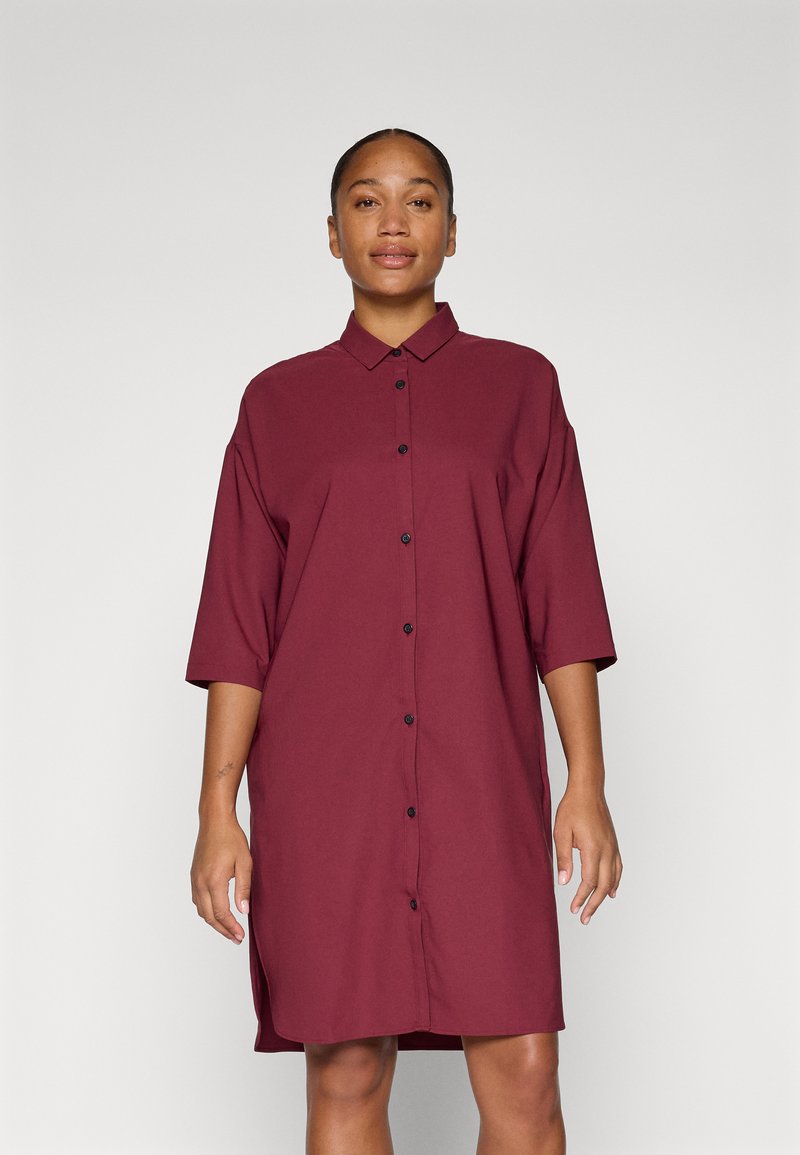 Vestido camisa burdeos con mangas cortas, un frente abotonado y un corte relajado. Fabricado en un tejido suave con sutil textura y con aberturas laterales.