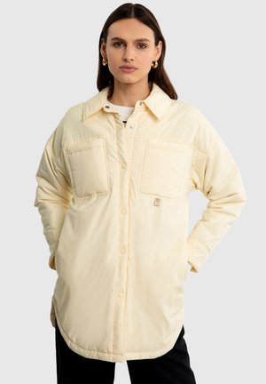 Pohodlná oversized košile-jacket v měkké světle žluté barvě, s knoflíkovou přední částí, dvěma náprsními kapsami a zakřiveným lemem.