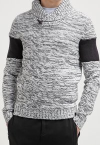 Grå och svart stickad tröja med krage, ribbad nederkant och strukturerad kropp. Har solida svarta detaljer på ärmarna.