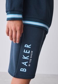 Marineblå tekstureret sweatshirt med blå stribede manchetter og matchende shorts med broderet "BAKER by TED BAKER" i lyseblåt på benet.