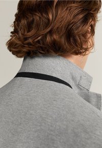 Grijze sweatvest met een hoge kraag en een zwarte accentstreep. Zachte textuur, casual ontwerp en minimale zichtbare stikdetails.