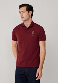 Burgundské polo tričko vyrobené z bavlny, s krátkym golierom a vyšitým logom. Slim fit s krátkymi rukávmi a bez viditeľných vzorov.