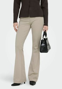 Pantalon beige évasé à texture lisse, accompagné d'un sac à main synthétique noir avec un motif crocodile et des ferrures argentées.