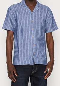 Korte mouw blouse in blauw met witte verticale strepen. Voorzien van een campkraag en houten knopen. Gestructureerde stof.