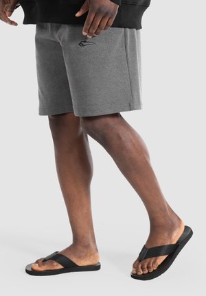 Shorts in cotone grigio con tasche laterali e un sottile logo nero, abbinati a ciabatte nere con cinturini testurizzati e suole piatte.