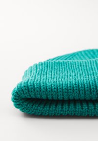 Teal knit beanie showing a ribbed texture, folded at the hem, with soft yarn creating a thick, warm appearance.