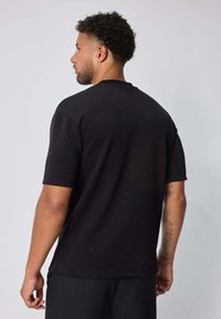 T-shirt noir à manches courtes, tissu texturé avec de petits points dispersés, encolure arrondie et coupe décontractée, vu de dos.