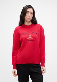Rød strikket sweater med rund hals, udstyret med broderet "New Haven" tekst og et logo. Ribbet manchetter og bund, glat tekstur.