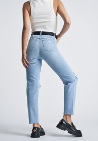 Light blue denim jeans with a straight cut, featuring distressed knees and a high waist. Back pockets have a diamond logo detail.