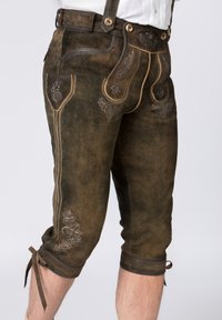 Braune Lederhosen mit detaillierter floralem Stickerei, Schulterträgern und Knöchelbindern. Die Textur ist glatt mit genähten Akzenten.