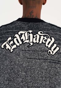Pletený svetr s černobílým barevným vzorem. Na zadní straně se nachází velká výšivka "Ed Hardy" v stylizovaném písmu.
