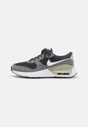 Grijze en zwarte Nike Air Max sneaker met witte swoosh, zichtbare luchtkussen in de zool en veterontwerp op een effen achtergrond.
