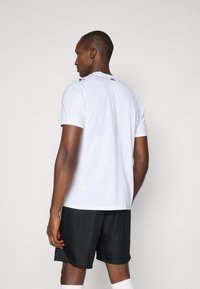 Hvit atletisk T-skjorte med korte ermer, med en subtil tekstur og kontrasterende svarte detaljer, sammen med svarte shorts. Enkel design.