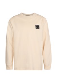 Maglietta in cotone beige a maniche lunghe con scollo rotondo e una toppa nera quadrata con dettaglio grafico circolare sul lato sinistro del petto.