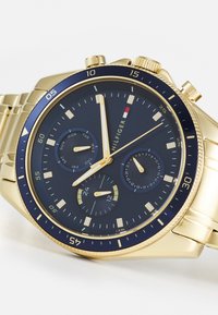 Goldfarbene Chronographuhr mit blauem Ziffernblatt, drei Hilfszifferblättern, strukturierten Indizes und einem Edelstahlarmband. Verfügt über eine drehbare Lünette.
