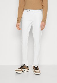 Pantaloni bianchi su misura con una texture liscia e una vestibilità slim. Indossati con sneakers marroni e crema, che aggiungono contrasto all'outfit.