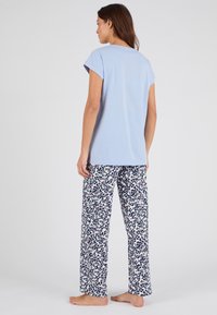 Camiseta de algodón azul claro con mangas cortas enrolladas, combinada con pantalones blancos que presentan un patrón abstracto de manchas multicolores.