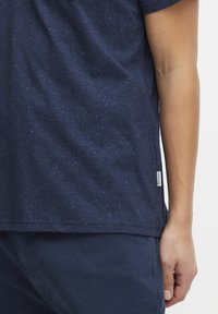 Námorně modré bavlněné tričko s tečkovanou texturou, s rovnými lemy a malou logo nášivkou na dolním levém rohu.