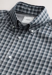 Košeľa s krátkym rukávom na gombíky v tmavomodrom a sivom károvanom vzore, s ostrým golierom a jemnou štítkovou značkou na ľavej strane hrude. Bavlnená látka.