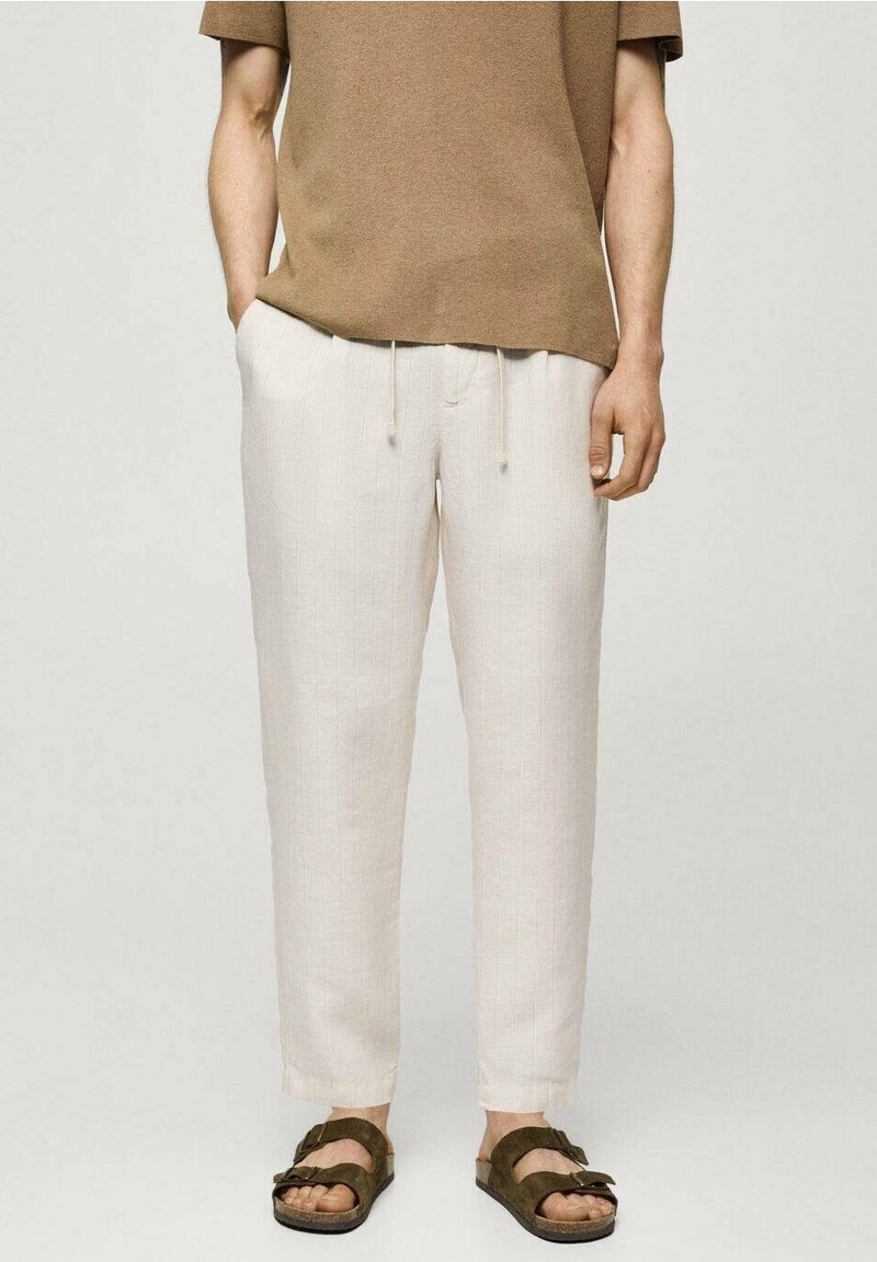 Svetle béžové kalhoty na stažení s texturovaným, žebrovaným vzorem, zkombinované s hnědým topem s krátkým rukávem a hnědými sandály.