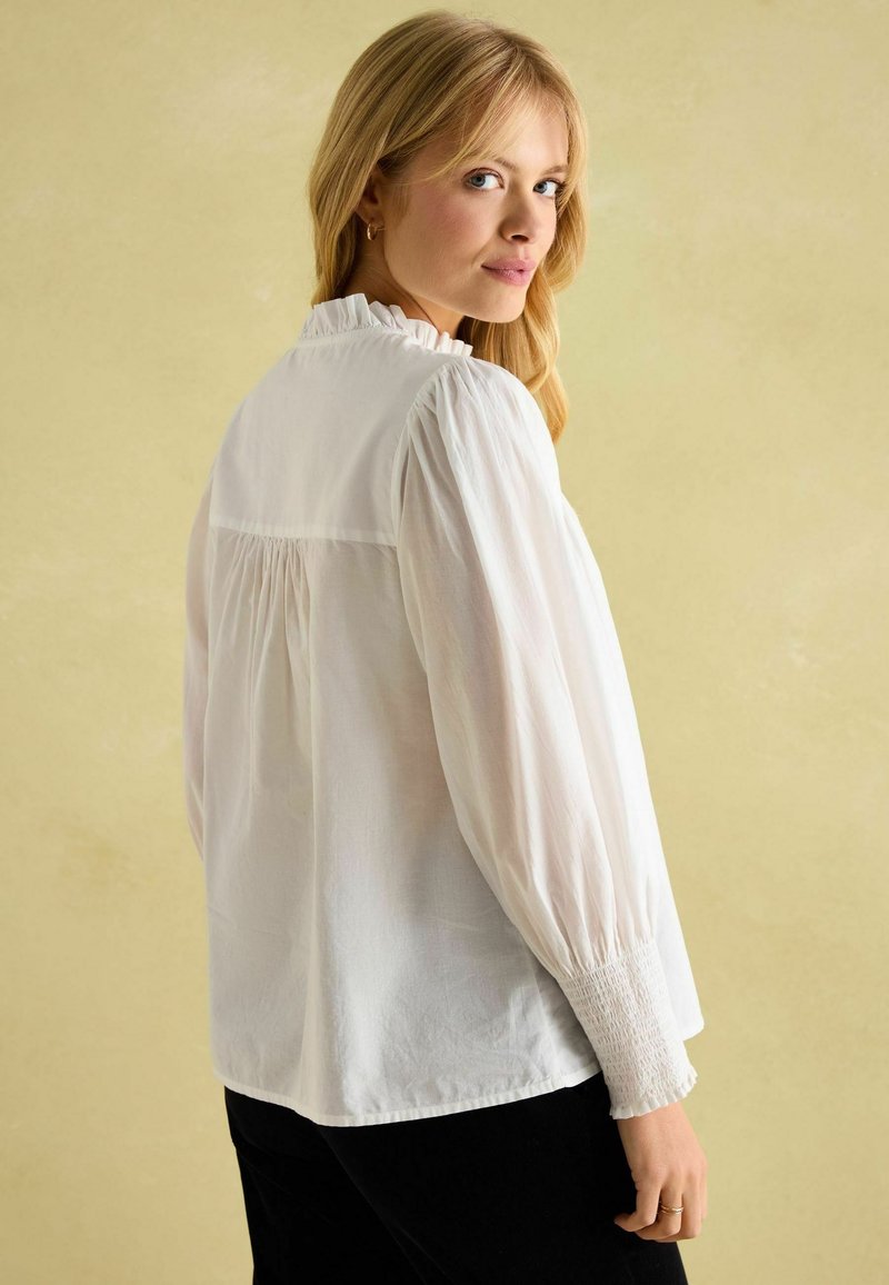 Weiße Bluse mit langen Ärmeln, Rüschkragen, gerafftem Rücken und gerüschten Manschetten. Glatte Textur und lockere Passform.