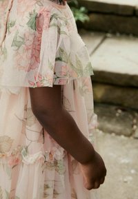 Robe florale en tulle rose clair avec des manches transparentes à volants. Présente des fleurs pastel et des feuilles, des jupes superposées avec des finitions délicates.