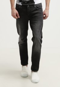 Černé džíny z denimu s úzkým střihem, pěti kapsami a jemným vyblednutím. Nošeny s bílými slip-on botami.