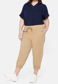 Námořnický krátký rukáv top s výstřihem do V; béžové lehké tapered kalhoty s elastickým pasem a šňůrkou. Bílé tenisky dotvářejí outfit.