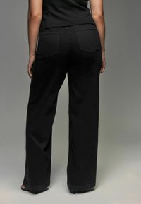 Zwarte, wijde jeans van denim met twee achterzakken en een hoge taille. De stof heeft een zachte textuur.