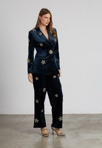 Conjunto de blazer y pantalones de terciopelo azul marino con embellishments florales, que presenta un diseño de doble botonadura, una textura suave y acentos plateados en contraste.