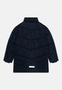Mornarska pufferska jakna z visokim ovratnikom, ki ima chevron prešito oblazinjeno teksturo, dolge rokave in belo oznako na zadnjem robu. Gladek, trpežen material.