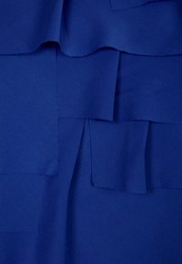 Tela azul con parches superpuestos de varios tamaños, creando un aspecto texturizado. El material parece suave con un ligero brillo.