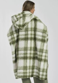 Groen en wit geruit deken met capuchon, voorzien van een zachte, fuzzy textuur, met grote ruiten en een losse, oversized ontwerp.