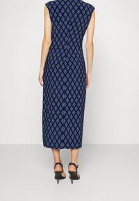 Robe sans manches bleu marine avec un motif en diamant bleu clair, longueur genou, avec une silhouette ajustée et une fente sur le côté, accompagnée de talons noirs.