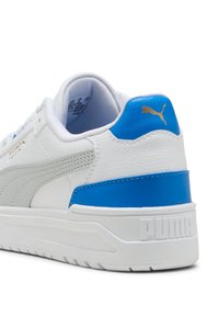 Weißer Sneaker mit blauen Akzenten, ausgestattet mit einem strukturierten Obermaterial, gepolstertem Kragen und einem goldenen Logo. Gummisohle mit markantem Profil.