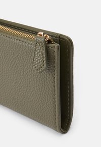 Portefeuille en cuir vert olive avec une finition texturée, doté d'une fermeture éclair et d'un onglet dorés. Design compact et rectangulaire aux bords nets.