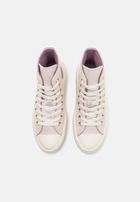 High-top sneakers with a cream canvas upper, lavender accents, white laces, and gold eyelets. Rounded toe and textured fabric panels.