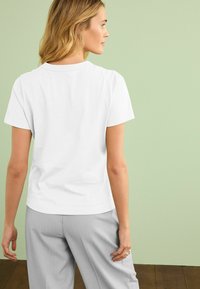 White short-sleeve T-shirt with a crew neckline, smooth cotton fabric, relaxed fit, paired with light grey wide-leg pants.