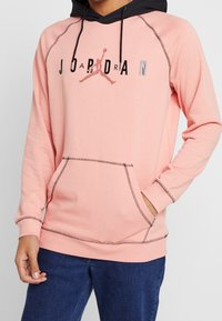 Felpa rosa chiaro con cappuccio nero, dotata di una tasca frontale e logo Jordan. Le cuciture a contrasto aggiungono dettagli al design.