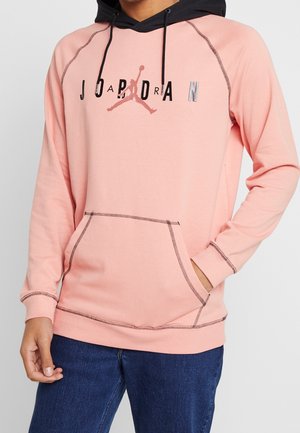 Sudadera rosa claro con capucha negra, con un bolsillo frontal y el logo de Jordan. La costura en contraste añade detalle al diseño.
