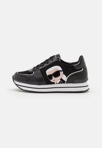 Zapatilla negra con un acabado brillante, que presenta una figura de dibujos animados con gafas de sol y cabello blanco en el lado, complementada con rayas blancas y negras.