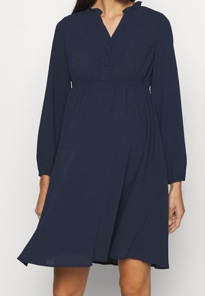 Woman wearing a navy blue knee-length dress with long sleeves, buttoned V-neck, gathered waist, and a slightly flared skirt.