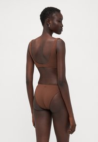 Brown ribbed bikini with wide straps and high-waisted bottom. Textured fabric with a subtle chevron pattern. Minimalist design, no hardware.