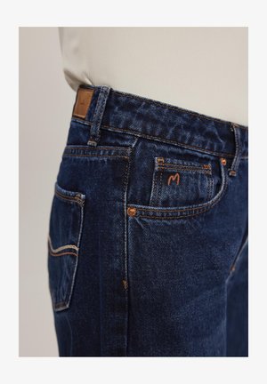 Ciemnoniebieskie dżinsy o zwężanym kroju z kontrastowym pomarańczowym przeszyciem, pięcioma kieszeniami i skórzaną metką na pasie.