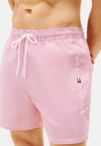 Shorts de bain rayés rouges et blancs avec une taille élastique et un cordon de serrage. Présente un logo imprimé sur le côté et une texture de tissu léger.