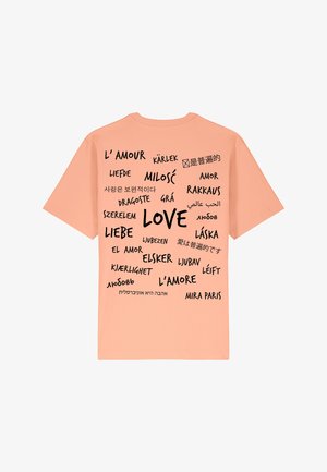 T-shirt de couleur pêche avec le mot "AMOUR" en lettres noires en gras, entouré de traductions en différentes langues. À manches courtes et décontracté.