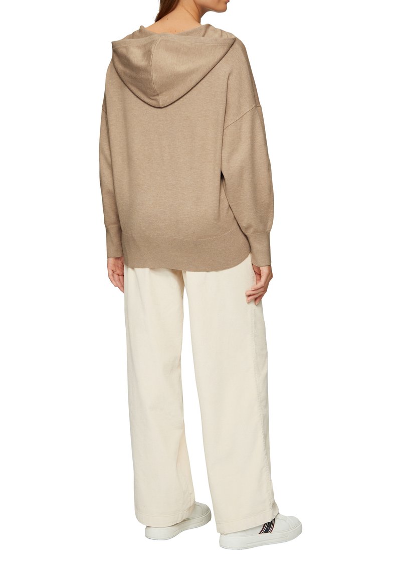 Beige Übergröße Hoodie aus weichem Material mit Kapuze, kombiniert mit locker sitzenden hellbeigen Hosen und weißen Sneakers.