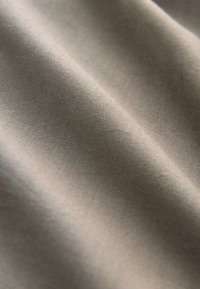 Tissu en coton beige avec une texture lisse, présentant des plis doux et un léger brillant. Vue en gros plan mettant en valeur le tissage fin et la douceur.