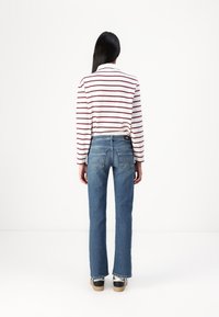 Camisa de rayas de manga larga en blanco y rojo, combinada con jeans azules. Los jeans tienen un ligero acampanado y bolsillos traseros con detalles de costura visibles.